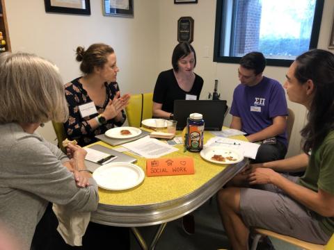 students and faculty sit at a yellow table talking