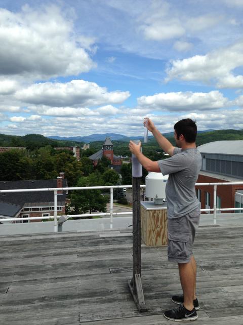 A male student stands atop the Boyd Science Center using a rain gauge.