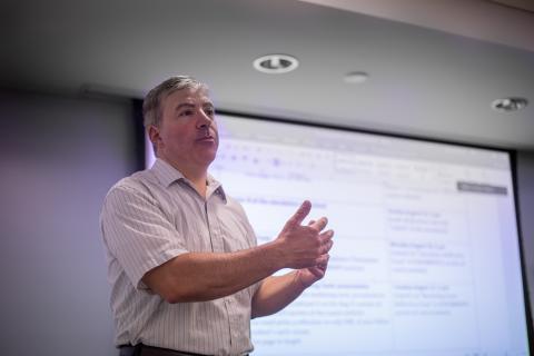 A man, George Pettinico, standing at the front of a classroom, mid-lecture