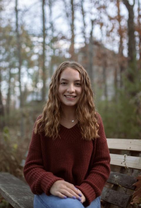 Photo of a girl, Hayley Neilson, sitting on a bench with trees behind her.