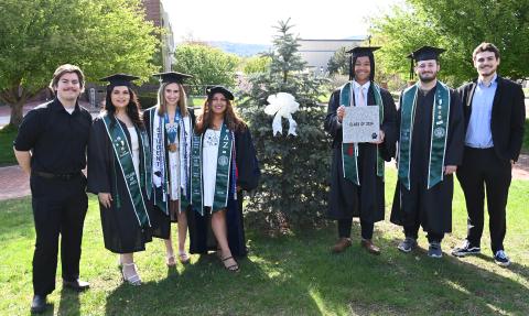 Photo of seven PSU students, some in their caps and gowns at graduation.