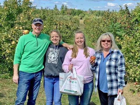 A photo of a man, Jack Cunnane, next to his wife and 2 daughters, standing in an apple orchard