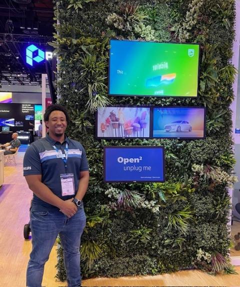 Photo of a man, Elijah Johnson, standing next to some tv displays at a professional conference